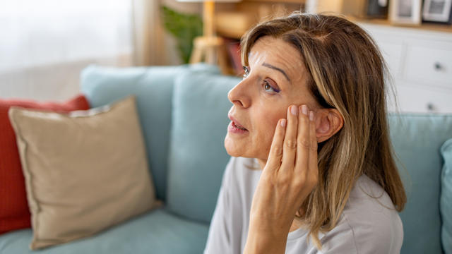 Older woman at home holding hand hear ear with expression of discomfort. 