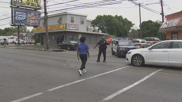 A police officer holds up a stop sign while a young person crosses the street in Darby 