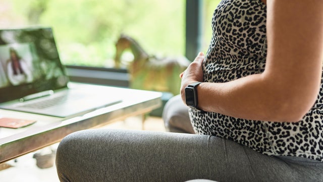 Heavily pregnant woman touching baby bump during online doula session 