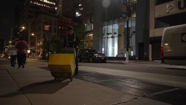 A deliveryman pushes a cart full of boxes along a New York City sidewalk at night. 