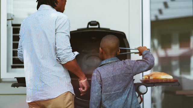 Young boy learning to barbecue with his dad rear view 