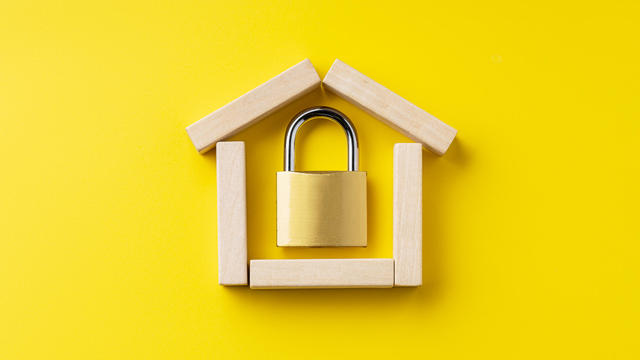 house symbol made by wooden blocks over yellow background with padlock inside. outer space. home protection and security concept 
