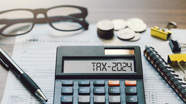 Word Tax 2024 on the calculator. Business and tax concept.Calculator, coins, book, tax form, and pen on table.Tax deduction planning.Financial research, government taxes, and calculation tax return