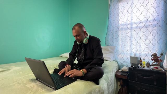 Naryndra "Roshan" Shiwcharran sits on his bed and works on his laptop. 