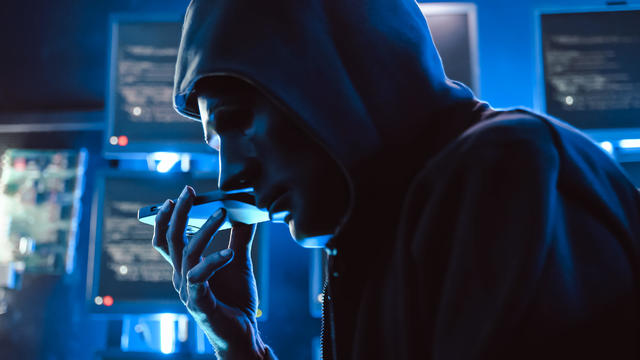 A hacker wearing a mask to cover his face is using computer to hack data to get ransom from victims. 