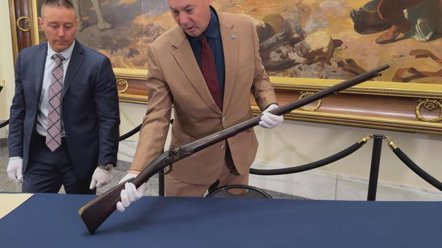 An expert wearing white gloves holds a long gun from the Revolutionary War 