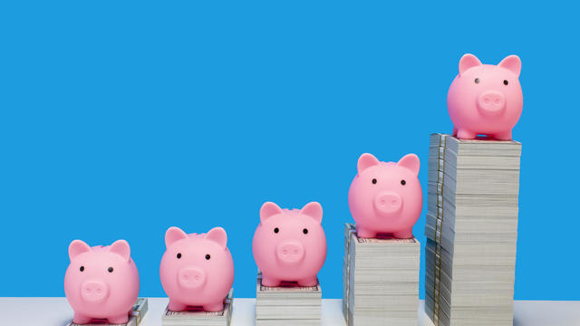 Pink piggy banks on ascending stacks of paper currency 