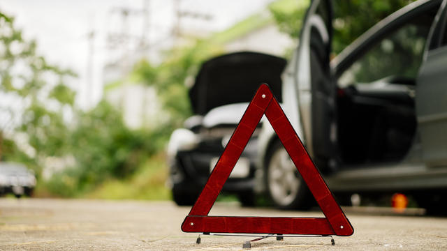 insurance adjuster claim a  Man in a safety vest setting up a red warning triangle by a car, indicating a breakdown or roadside emergency. 