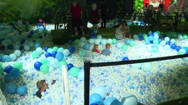 Children and adults play in a ball pit inside Balloon Story. 