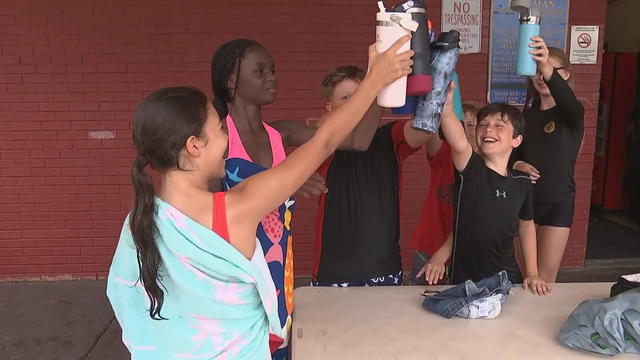 Kids raise their water bottles in a toast after getting out of a pool 