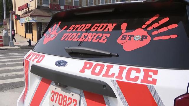 AN NYPD vehicle with orange stripes on it and an orange decal on the rear windshield with two handprints and the words "Stop Gun Violence." 