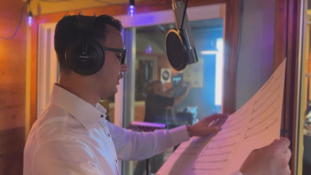Brandon Tomasello reads from sheet music as he records a song in a studio 