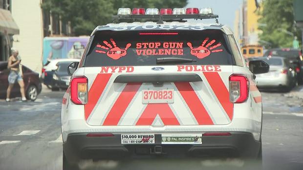 AN NYPD vehicle with orange stripes on it and an orange decal on the rear windshield with two handprints and the words "Stop Gun Violence." 