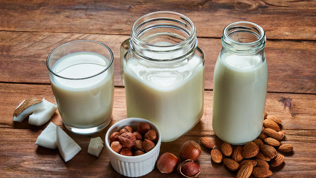 Alternative types of vegan milks in glass bottles on rustic wooden table 