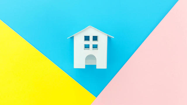 Simply design with miniature white toy house isolated on blue yellow pink pastel colorful trendy geometric background Mortgage property insurance dream home concept. Flat lay top view copy space 