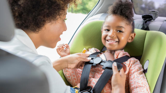 Little girl smiles as she is buckled into car seat 