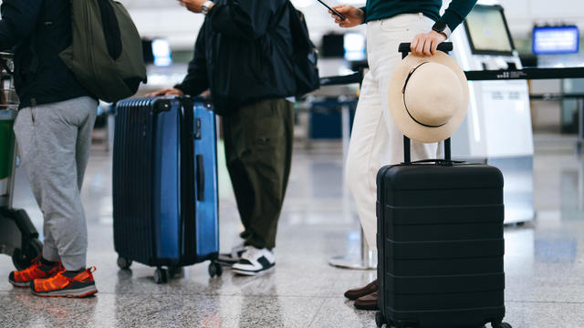Cropped shot of group of airline passengers with suitcases standing in queue, waiting at check-in counter at International airport. Ready for a trip. Business travel. Travel and vacation concept 