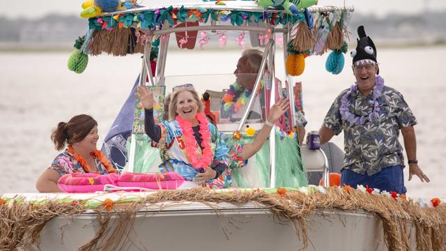 People wave from a boat decorated for the theme "Summertime Vibes" 