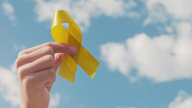 Hands holding yellow gold ribbon over blue sky, Sarcoma Awareness, Bone cancer, childhood cancer awareness, September yellow, World Suicide Prevention Day concept 