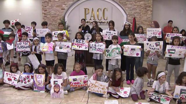 Dozens of children stand in the Palestinian American Community Center holding handmade signs calling for a cease-fire and free Palestine. 