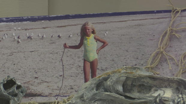 A photo from the exhibit, it shows Taylor Swift as a child standing on the beach holding a stick 