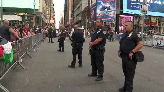Several NYPD officers stand in a street in Times Square as protesters gather behind barricades. 
