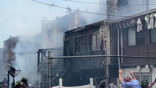 Dozens of FDNY officials stand outside a Queens Village home that has suffered fire damage. 