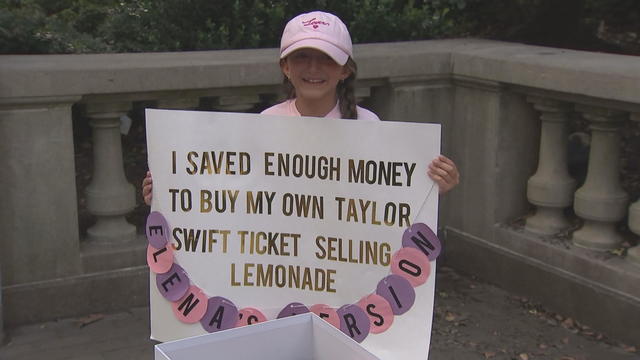 Elena holds up a sign that says I saved enough money to buy my own Taylor Swift ticket selling lemonade 