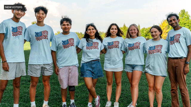 A group of young people post for a photo, they're wearing matching shirts with American flags on them 