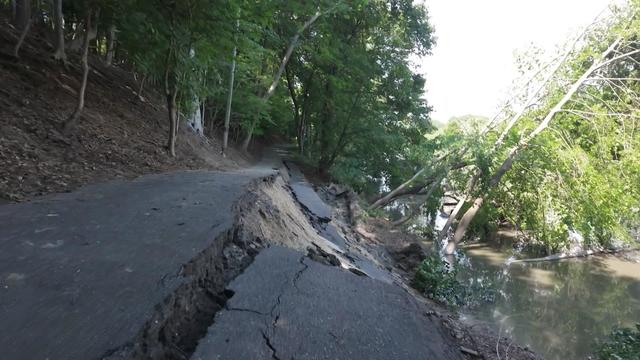 A roadway that has partially collapsed into a body of water below. 