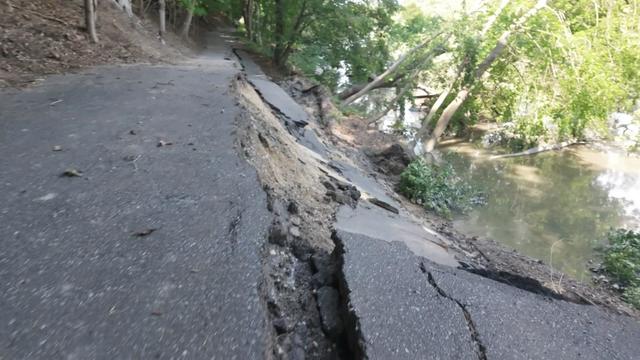 A roadway that has partially collapsed into a body of water below. 