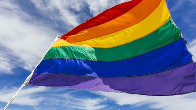 Rainbow flag waiving in the wind against blue sky 