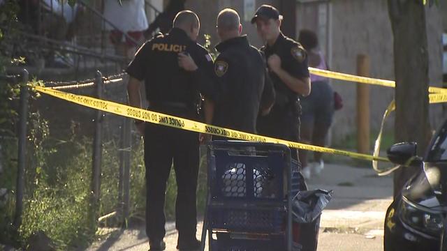 Police officers stand on the sidewalk outside a Paterson home. 