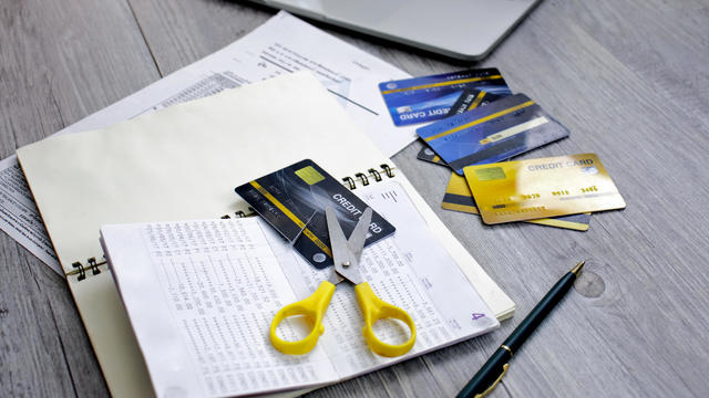 Credit card cut with scissors placed on a table with laptops and bills 