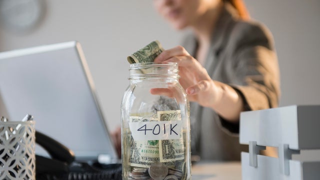 Businesswoman putting money into 401K jar at desk