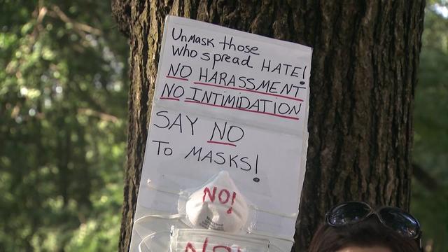 A protest sign reading, "Unmask those who spread HATE! NO HARASSMENT. NO INTIMIDATION. SAY NO To MASKS!" Below the writing are two medical face masks with the word "NO!" written on each. 