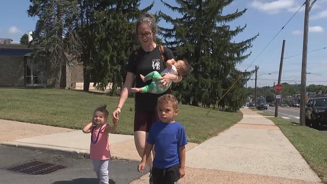 A mother walks on a sidewalk with her three children 