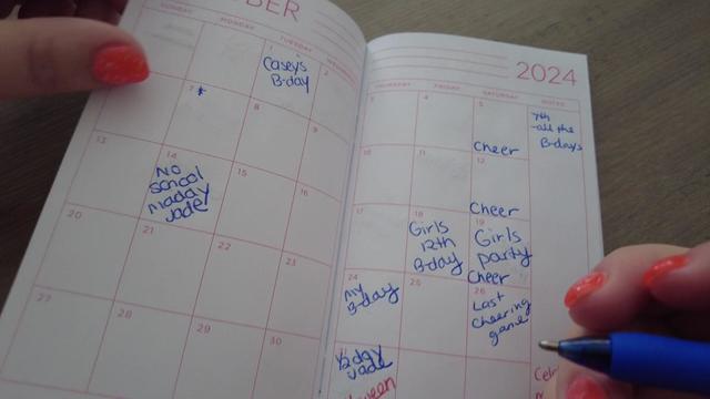 A mother fills her October 2024 calendar book with birthdays and school activities. 