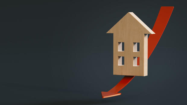 Stylized model of a wooden house slides a red arrow down on a dark background with space for text or logo. 3D rendering. Falling real estate prices 