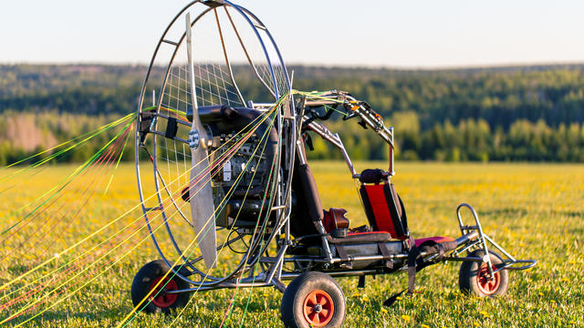 Paragliding machine for paragliding flights on green grass against the bright sun. Preparing paralet with a gasoline engine for flights. Extreme sports 