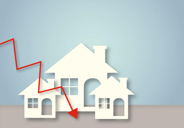 White paper houses with red arrow down on wall background. Concept for low cost real estate. 