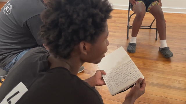 A teen leans forward while reading from his travel journal 