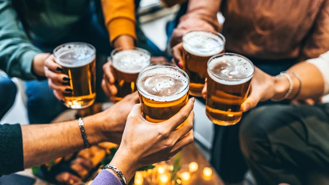 Group of friends drinking and toasting glass of beer at brewery pub restaurant- Happy multiracial people enjoying happy hour with pint sitting at bar table- Youth Food and beverage lifestyle concept