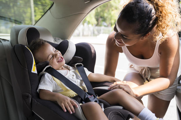 Baby girl smiles as she is buckled into car seat. 