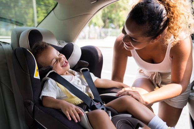 Baby girl smiles as she is buckled into car seat.