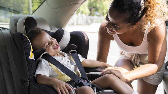 Baby girl smiles as she is buckled into car seat. 