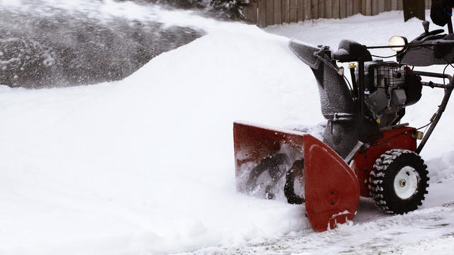 Close-up of red snowblower clearing snow-filled lane 