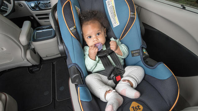 Baby girl smiles as she is buckled into car seat. 