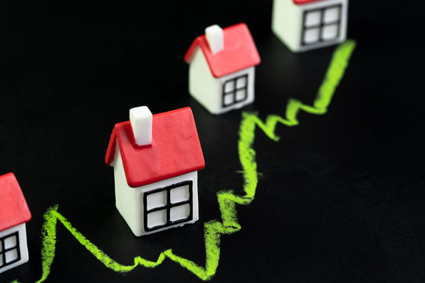 House, property or real estate market price go up or rising concept, small miniature house with green line graph going up on black chalkboard 