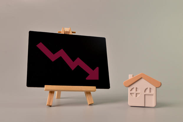 Toy house and arrow down drawn on chalkboard. Falling real estate prices market 